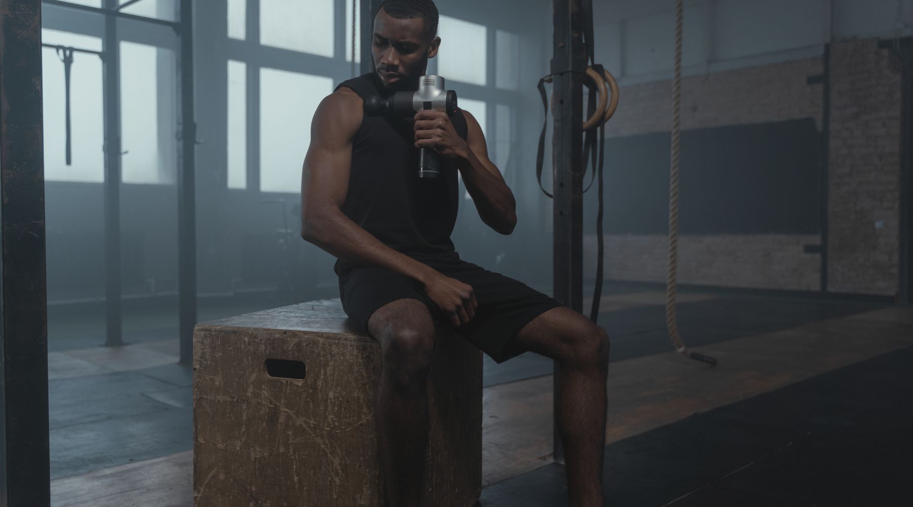 Fit male athlete using a percussive massage gun on his shoulder for muscle recovery after a workout